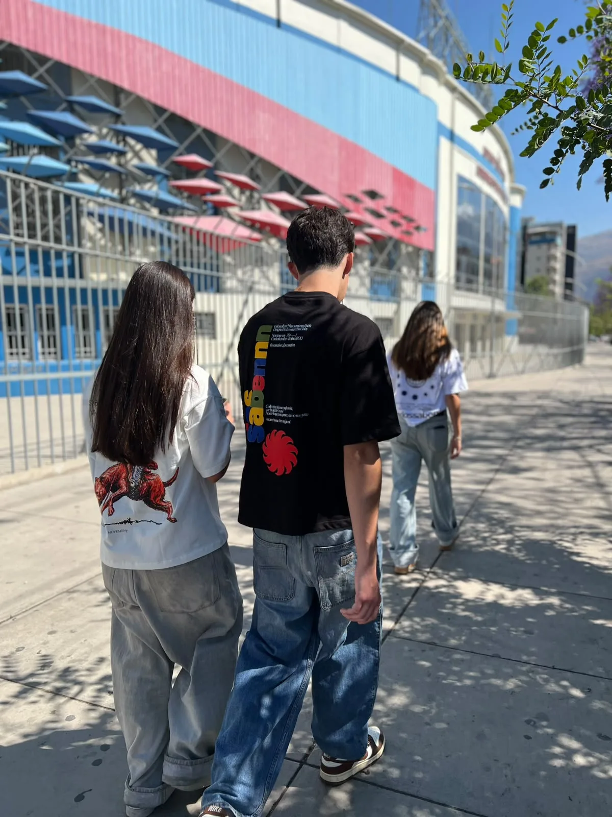 tres modelos de espaldas frente al estadio con las poleras JINETE, CLUBS y ESSENTIALS del drop-01